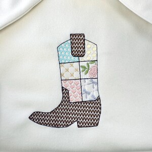May include: A brown and white embroidered boot with a patchwork design. The boot is made of fabric and has a pointed toe.