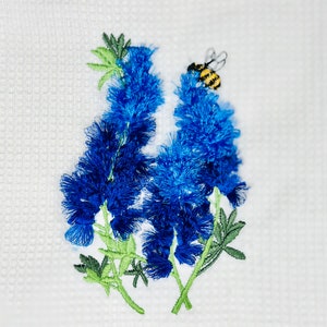 May include: Embroidered kitchen towel with a blue flower design and a bee. The towel is white with a waffle weave texture.