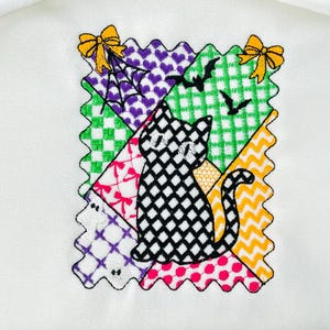 May include: Embroidered Halloween-themed patch featuring a black and white cat on a patchwork design. The patchwork includes purple hearts, green checks, and orange zigzags. Yellow bows and bats complete the design.