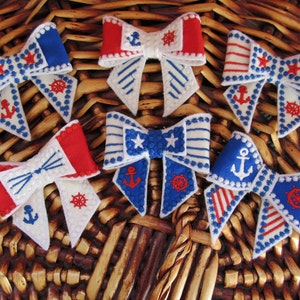 May include: Six handmade fabric bows in red, white and blue with nautical themed embroidery. The bows feature anchors, stars and steering wheels.