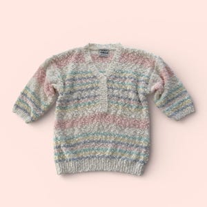 May include: A multi-colored sweater with a V-neck and three buttons. The sweater features horizontal stripes in pastel colors, including pink, blue, yellow, and white. The label reads "ALICE THOMAS".