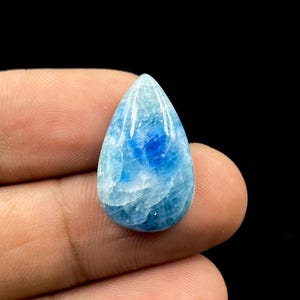 May include: A pear-shaped blue apatite gemstone with a smooth, polished surface. The stone displays a vibrant mix of translucent light blue and deep royal blue hues, featuring internal veining and a glossy finish that reflects light.