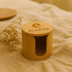 May include: A cylindrical bamboo container with a curved opening and a lid. The lid is engraved with the word "ELARZA" and a stylized design. The container is light brown and sits on a beige surface.