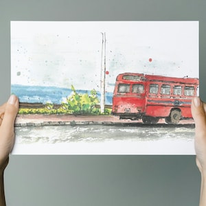 May include: Watercolour painting of a red bus on a street, with a coastal scene in the background. The bus has several windows and is set against a pale blue sky. The artwork is held by two hands.