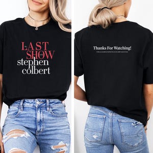May include: Black t-shirt featuring the text "the LAST SHOW with stephen colbert" in red and white. The back of the shirt displays "Thanks For Watching!" in white text. The shirt is paired with blue jeans.