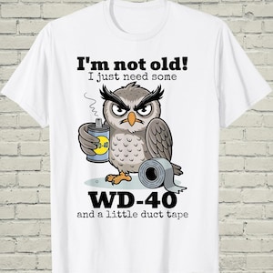 May include: White t-shirt featuring a cartoon owl holding a WD-40 can and duct tape. The text on the shirt reads "I'm not old! I just need some WD-40 and a little duct tape."