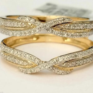 May include: A gold ring guard featuring two bands connected by a central crossover design. Both bands are encrusted with small, clear pavé-set stones that extend across the front, creating a continuous sparkling effect on the polished gold metal.