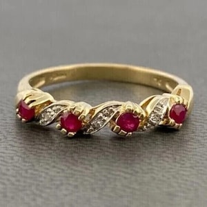 May include: A gold ring with a repeating pattern of red gemstones and small white gemstones. The ring has a delicate, elegant design, with the gemstones set in a wave-like pattern.