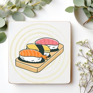 May include: Square coaster with a cartoon illustration of three sushi pieces on a wooden board. The sushi includes salmon, yellow, and tuna, set against a white backdrop with a yellow spiral design.