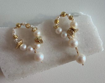 May include: A pair of earrings with white pearls and gold-coloured details. The earrings have a circular design with dangling pearl drops, creating a sophisticated and timeless look. The design is suitable for various occasions.