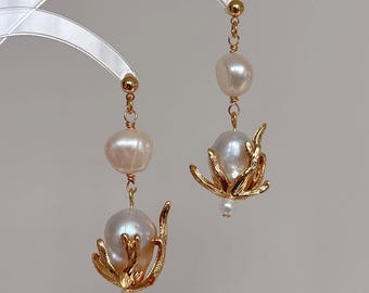 May include: Elegant gold-toned earrings featuring large, lustrous pearls. Each earring showcases a cluster of gold-colored, stylized floral elements cradling a pearl. The earrings hang from delicate gold chains, creating a sophisticated and eye-catching design.