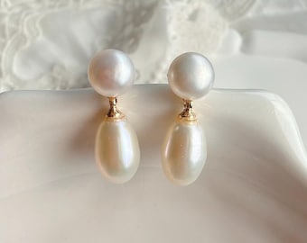 May include: A pair of drop earrings featuring a round white pearl at the top connected by a gold-toned metal post to a larger, elongated teardrop-shaped white pearl at the bottom. The pearls have a smooth, lustrous finish and a classic design.
