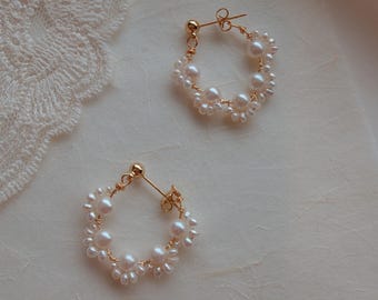 May include: A pair of gold hoop earrings featuring small white freshwater pearls wired along the circular frame. Each earring includes a gold post backing and a delicate arrangement of multiple pearls of varying sizes secured with thin gold wire.