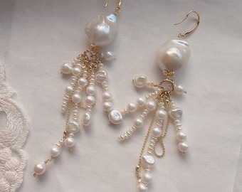 May include: A pair of elegant earrings featuring large, irregular white pearls suspended from gold-colored hooks. Smaller pearls and delicate gold chains cascade from the main pearl, creating a flowing, luxurious design. The earrings are set against a soft, white background.