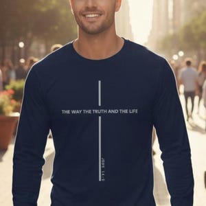 May include: Navy blue long-sleeve shirt with a vertical white cross design. The text "THE WAY THE TRUTH AND THE LIFE" is above the cross, with "JOHN 14:6" below. The shirt is a crew neck style.