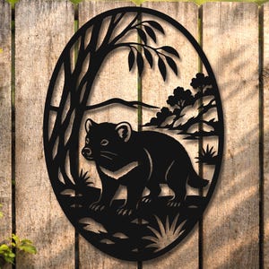 May include: Black metal wall art featuring a Tasmanian devil within an oval frame. The design includes a tree, foliage, and a landscape background. The artwork is mounted on a wooden fence.