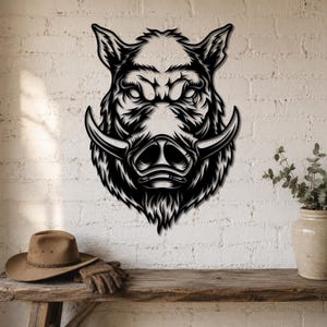 Könnte beinhalten: Ein Wandkunstobjekt aus schwarzem Metall mit einer detaillierten, stilisierten Illustration eines Wildschweinkopfes. Das Design zeigt scharfe, aggressive Gesichtszüge, markante, gebogene Stoßzähne und strukturierte Fellmuster in einer kontrastreichen Silhouette.