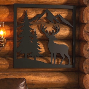 May include: Black metal wall art featuring a silhouette of a deer, pine trees, and mountains within a square frame. The artwork is mounted on a wooden wall, creating a rustic, nature-inspired aesthetic. A warm-toned lamp is visible on the left.