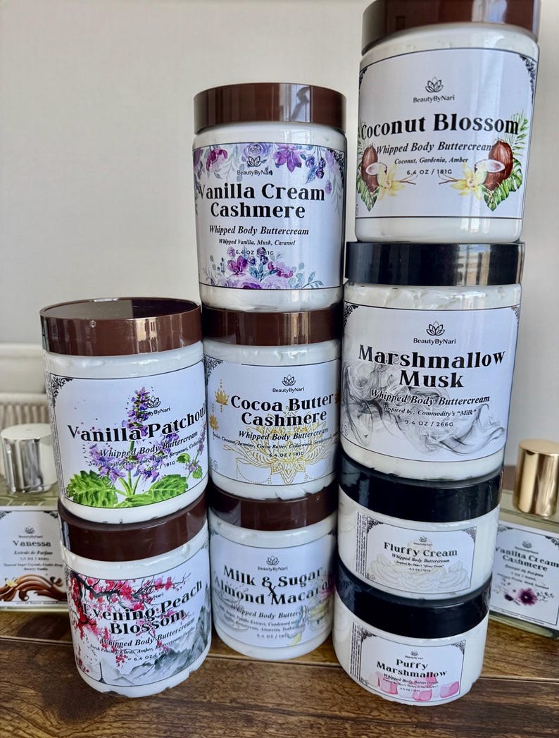 May include: A collection of whipped body buttercreams in various scents, displayed in white jars with brown lids. The labels feature floral designs and text such as "Vanilla Cream Cashmere" and "Coconut Blossom".