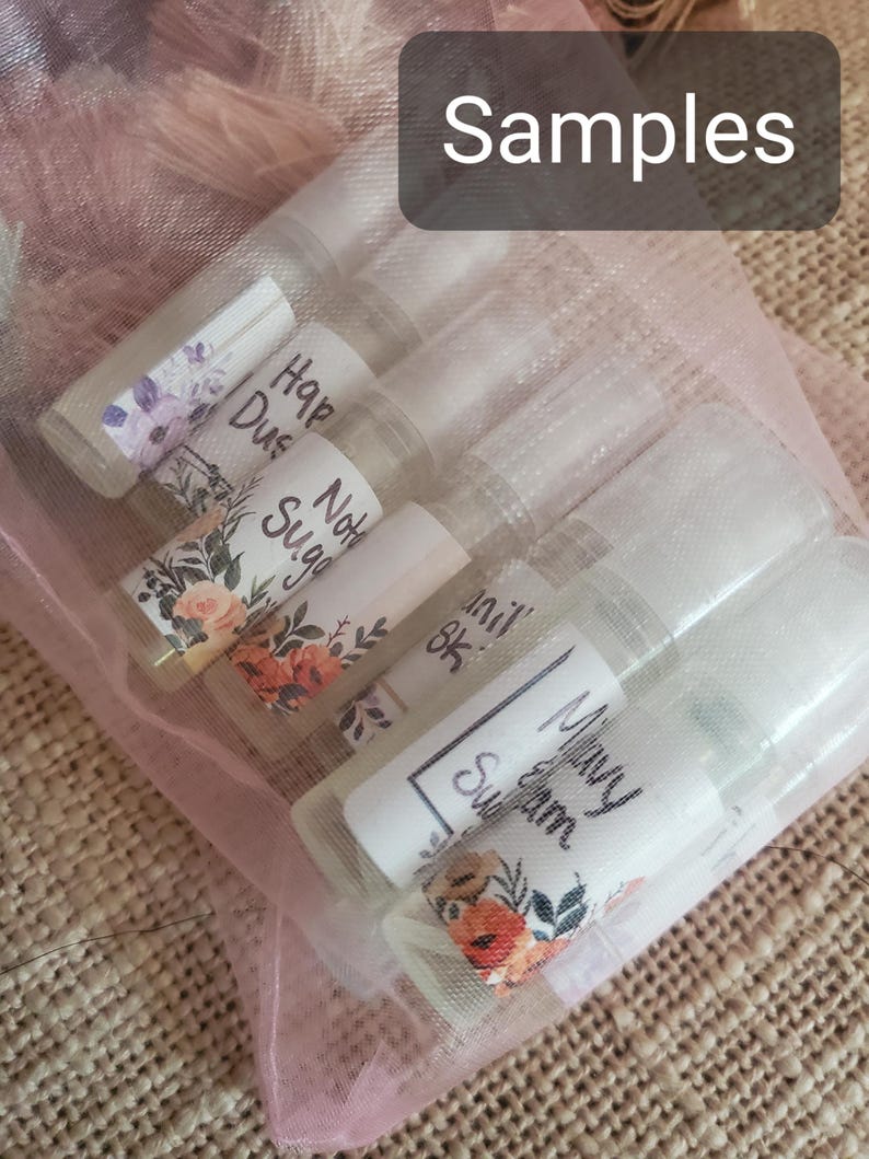 May include: A collection of small, clear sample bottles with white labels and floral designs, held in a sheer pink bag. The labels feature handwritten text, including the word "Samples" at the top.
