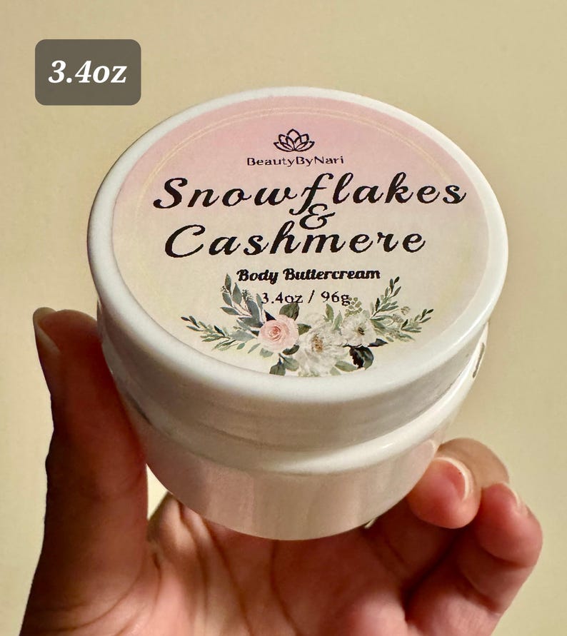 May include: A white jar of body buttercream with a floral design and the text "Snowflakes & Cashmere." The label also includes the text "Body Buttercream" and "3.4oz / 96g."