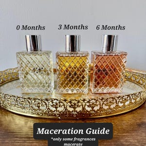 May include: Three perfume bottles with silver caps sit on a gold-rimmed tray. The bottles are labeled "0 Months", "3 Months", and "6 Months", showing the color change over time. The text "Maceration Guide" is below the bottles.