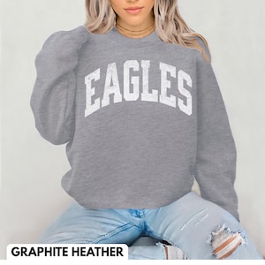 May include: A grey sweatshirt with the word "EAGLES" in large, distressed white letters across the chest. The sweatshirt has long sleeves and a crew neck. The text "GRAPHITE HEATHER" is at the bottom of the image.