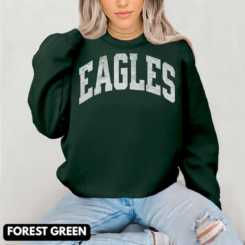 May include: Forest green sweatshirt featuring the word "EAGLES" in distressed white lettering. The sweatshirt has a crew neck and long sleeves. The text "FOREST GREEN" is displayed in a black rectangle at the bottom of the image.
