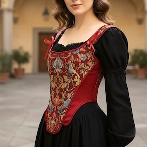 May include: A red and gold tapestry corset with a floral and bird design. The corset has a sweetheart neckline and red straps with small bows. The corset is worn over a black top and dress.