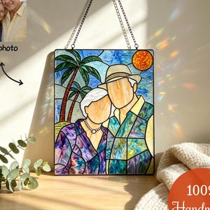 May include: A rectangular stained glass panel featuring a couple standing under palm trees with a sun in the background. The piece is rendered in shades of blue, green, purple, and orange, and is suspended by a black metal chain for wall display.