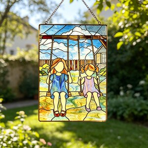 May include: A rectangular stained glass suncatcher featuring two figures on swings against a blue sky with white clouds. One figure wears a blue dress, the other a light purple dress. The scene includes a wooden fence and green foliage.