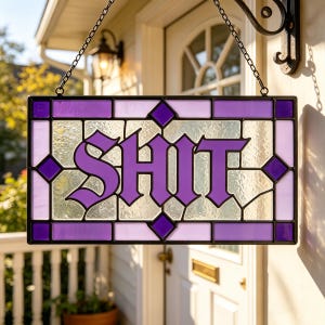 May include: A rectangular stained glass hanging sign featuring the word SHIT in bold purple lettering. The piece is constructed with a black metal frame and a mix of textured clear, light lavender, and deep purple glass panels held by chains.