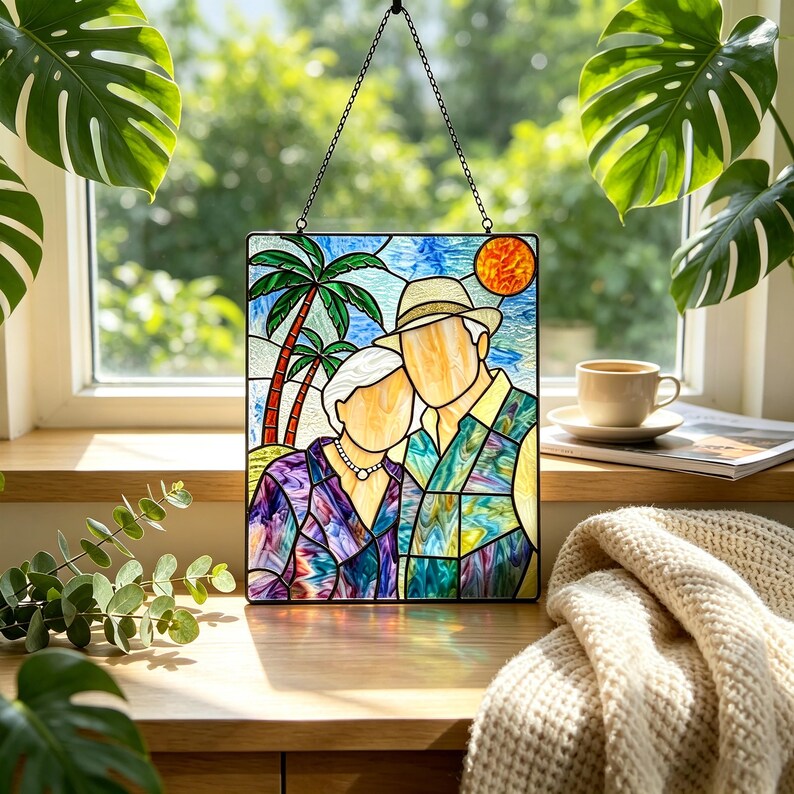May include: A rectangular stained glass suncatcher featuring a faceless couple standing before palm trees and a bright orange sun. The person on the left wears a purple patterned shirt and necklace, while the person on the right wears a hat and a blue and green patterned shirt. The piece is suspended by a black metal chain.