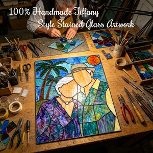 May include: A stained glass artwork depicting a couple standing under palm trees with a sun in the sky. The piece features a variety of colored glass segments joined by metal lines. The text 100% Handmade Tiffany Style Stained Glass Artwork is visible.