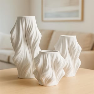 May include: Three white ceramic vases with a draped fabric design. The vases vary in size, with the tallest one standing approximately 12 inches tall. The design gives the vases a unique, textured appearance, suitable for home decor.