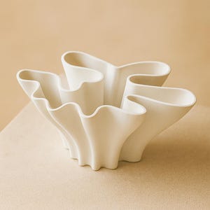 Peut inclure: Un bol décoratif en céramique blanche avec un design ondulé unique. Le bol présente plusieurs sections incurvées qui créent une forme ouverte et organique. Sa couleur neutre et son design moderne en font une pièce polyvalente.