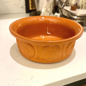 May include: An orange ceramic bowl with a floral pattern around the sides. The bowl has a glossy finish and a simple, rounded shape. The bowl is likely used for serving or display.