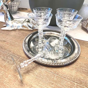 May include: A silver serving tray holds four clear champagne glasses with floral etching. A fifth glass lies on its side. A silver deer figurine and a candelabra are in the background. The items are on a wooden surface.