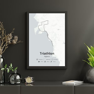 May include: A framed print featuring a map of a triathlon course in Alghero. The black and white design includes the word "Triathlon" and the location. The course details include distances for swimming, cycling, and running.
