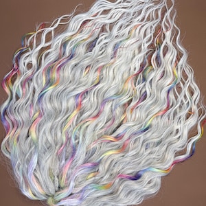 Può includere: Un fascio di extension per capelli lunghi e ondulati grigi con striature di colori arcobaleno. I capelli sono acconciati in onde sciolte, con le ciocche colorate sparse nel grigio. Lo sfondo è marrone pieno.