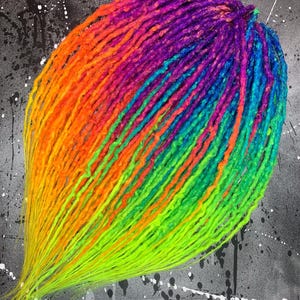 Puede incluir: Un conjunto de extensiones de rastas multicolores. Los colores van del amarillo al naranja, luego al rosa, morado, azul y finalmente al verde. El fondo es gris moteado con salpicaduras de pintura blanca.