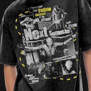 Op de afbeelding: Zwart grafisch t-shirt met een distressed design. Het shirt heeft de tekst "Next Semester" en andere zinnen, samen met afbeeldingen van mensen. Gele streepjes en tekst accentueren het ontwerp.