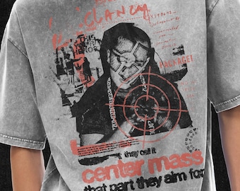 May include: Gray t-shirt with a graphic design featuring a person with a target over their face, and the words "CLAN" and "CENTER MASS" in red. The shirt also has the text "Twenty One Pilots" and other text.
