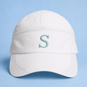 May include: White baseball cap featuring a teal embroidered letter "S". The cap has a curved peak and a structured design with a seam detail across the top. It has an adjustable strap at the back.