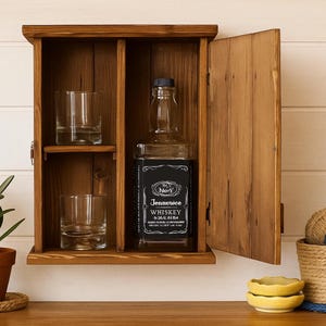 May include: A wooden cabinet with a hinged door, holding two clear glasses on a shelf, and a whiskey bottle. The cabinet is open, revealing the contents. A small potted plant and decorative items are on the table below.