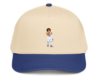 May include: A baseball cap with a cream-colored crown and a royal blue brim. The cap features a small graphic of a basketball player in a white jersey with the number 11. The cap has a blue button on top.