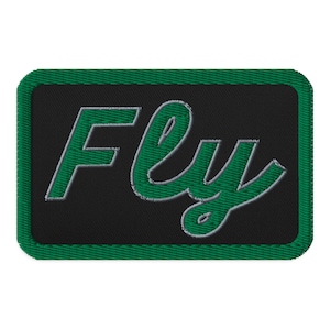 May include: Embroidered patch featuring the word "Fly" in green script with a white outline, on a black background. The patch has a green border and a rectangular shape.
