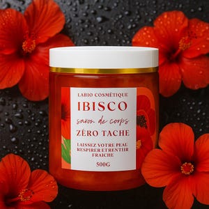 Könnte beinhalten: Ein Glas Körperseife mit weißem Deckel und goldenem Rand, beschriftet mit "IBISCO savon de corps ZÉRO TACHE" mit dem Text "LAISSEZ VOTRE PEAL RESPIRER ETRENTIIR FRAICHE" und "500G". Das Glas ist von leuchtend roten Hibiskusblüten umgeben.