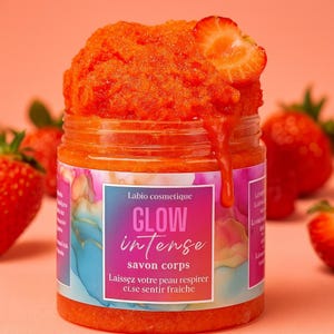 Könnte beinhalten: Ein Glas mit orangefarbenem Körperpeeling und einer Erdbeerscheibe obenauf. Auf dem Etikett steht "Labio cosmetique GLOW intense savon corps". Erdbeeren sind um das Glas herum auf einem rosa Hintergrund verstreut.
