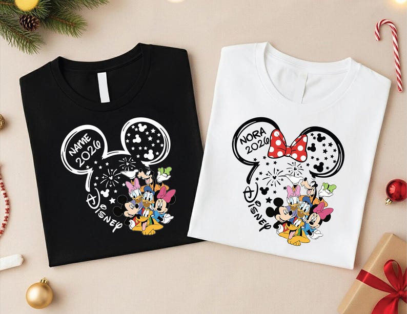 two t-shirts with Disney-themed designs, including Mickey Mouse and Minnie Mouse characters. The t-shirts are placed on a surface with Christmas decorations, such as ornaments and a Christmas tree.